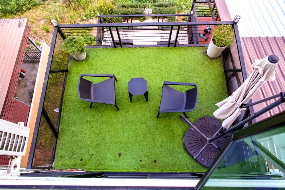 A bird’s eye view of artificial grass on a balcony with chairs and an umbrella.
