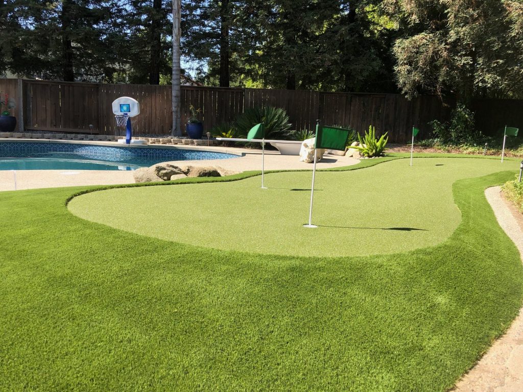 An artificial putting green in a Fresno backyard with a pool.